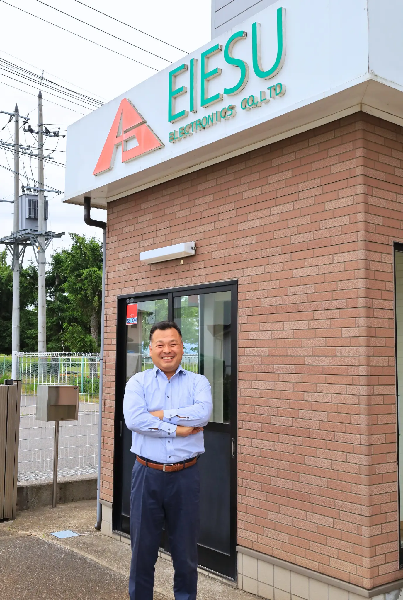 代表取締役 荻原 栄一 - 会津事業所前に立つ