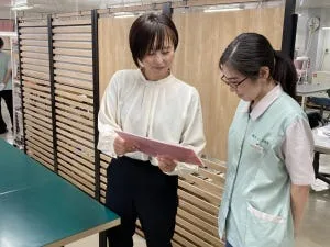 紙の資料を見ながら話す2人の女性。1人は薄緑の作業服を着ている